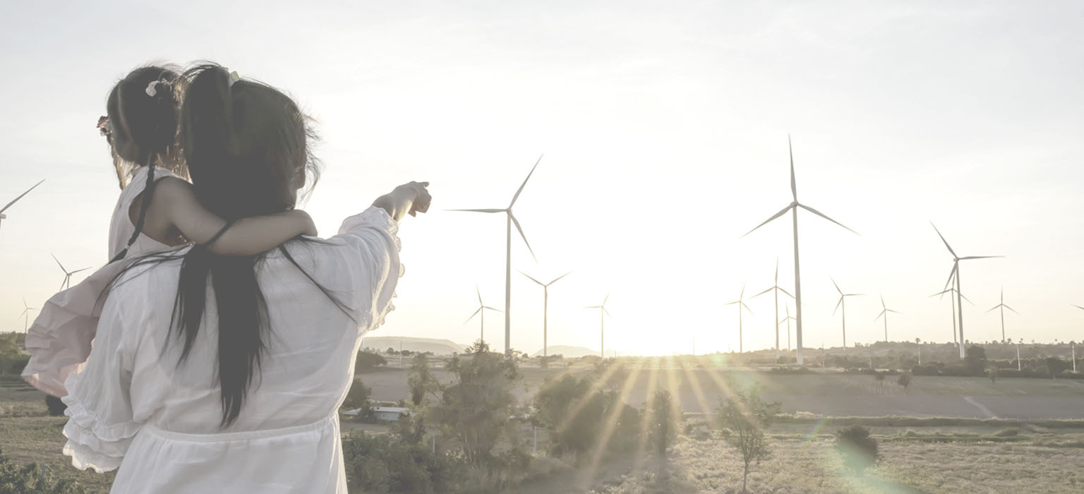 A woman holds a young girl and points to a wind farm on the horizon